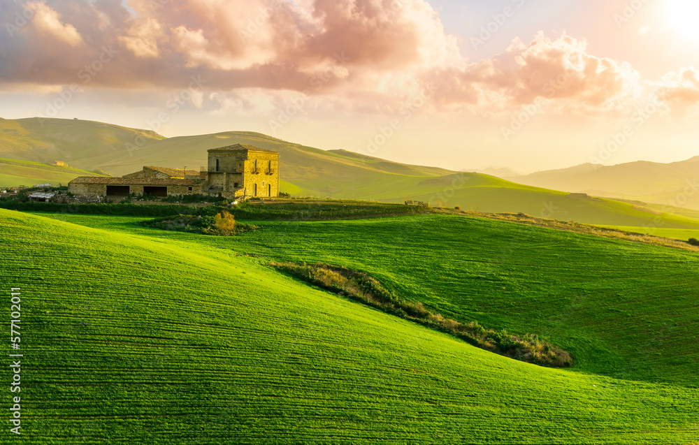 sceniv view at a nice farm in green fields in hills and highlands, landscape of spring green hills with mountain bright sunset on backdrop