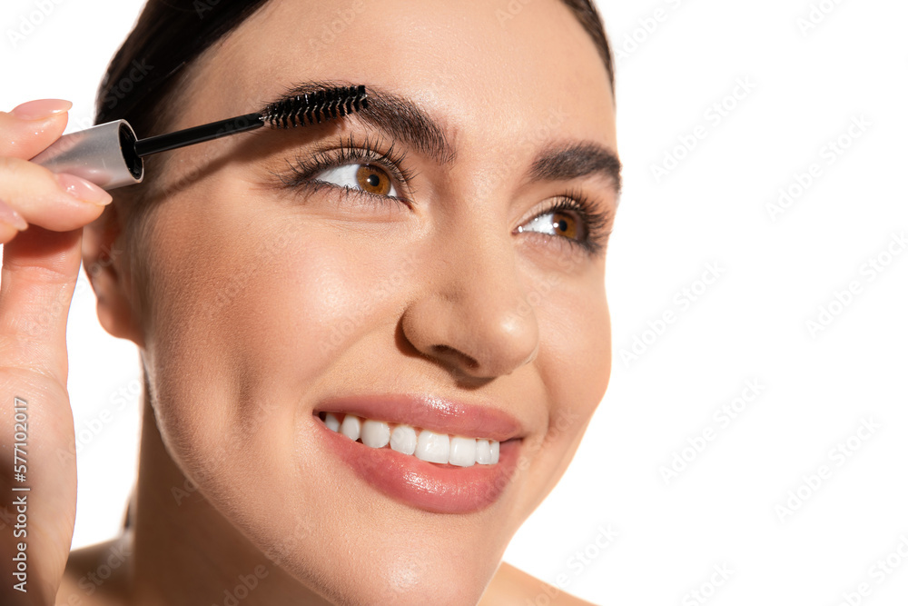 close up of happy young woman holding brush and styling eyebrows with gel isolated on white.