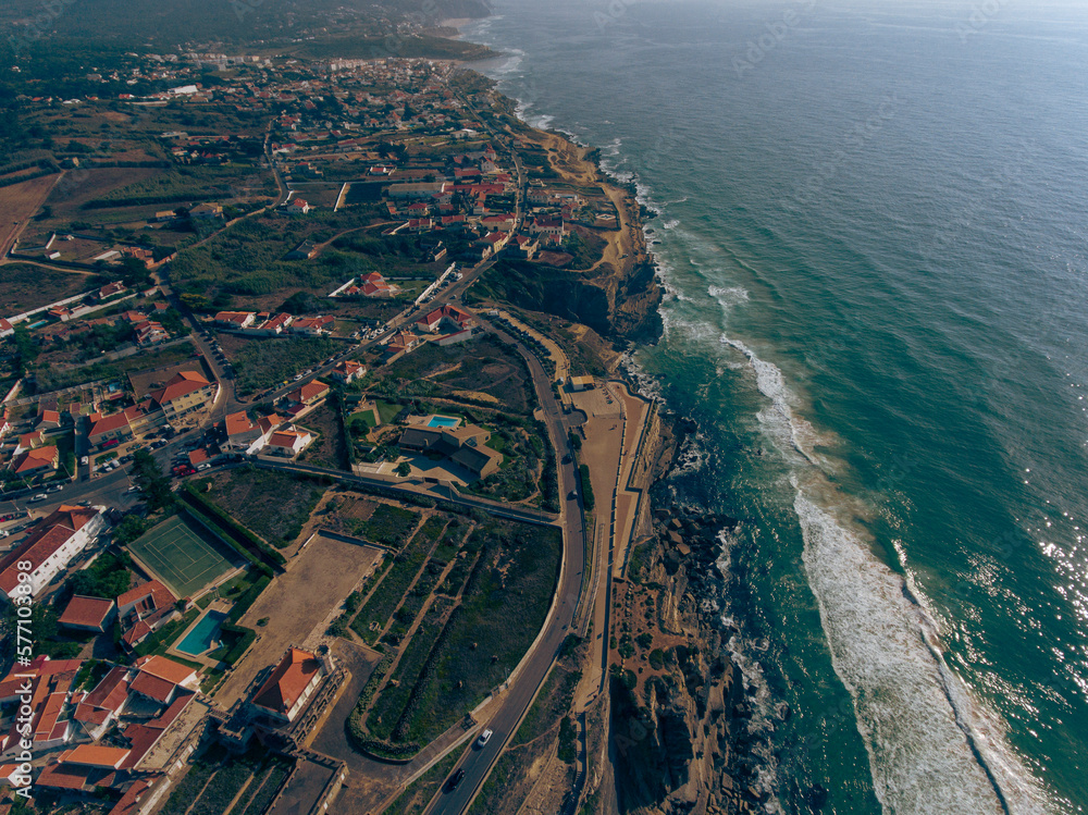 Fototapeta premium Aerial photos of Azenhas do Mar in Sintra, Portugal showcase a picturesque seaside village with white houses and a natural swimming pool, surrounded by dramatic cliffs and the sparkling Atlantic Ocean