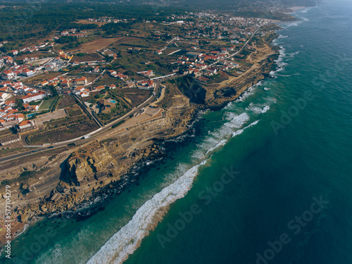 Aerial photos of Azenhas do Mar in Sintra, Portugal showcase a picturesque seaside village with white houses and a natural swimming pool, surrounded by dramatic cliffs and the sparkling Atlantic Ocean