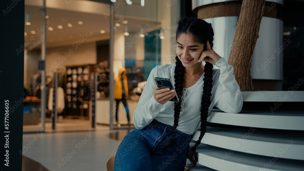 Fototapeta premium Female student middle-eastern girl businesswoman arabian ethnic woman student shopper chatting on phone sit at shopping center use mobile apps purchasing online read digital news watch internet video