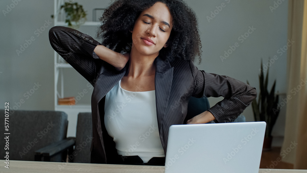Tired exhausted african woman businesswoman employee sit at office desk feel back muscle tension fatigue after computer work massaging neck relieve spine spasm doing healthy body gymnastic relaxation - obrazy, fototapety, plakaty 