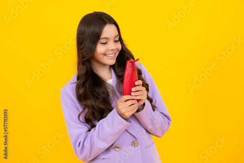Teen child girl with shampoo bottle or shower gel isolated on yellow background. Kids hair cosmetic product. Happy teenager, positive and smiling emotions of teen girl.