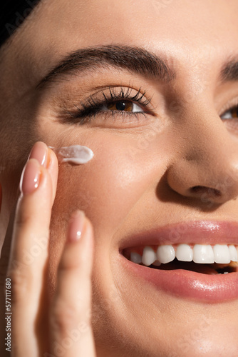 Foto close up view of joyful young woman applying cream on cheek.