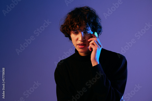 Man with phone in hand teenager online video call and selfies, hipster lifestyle blogger, portrait purple background, mixed neon light, fashion style and trends, copy space