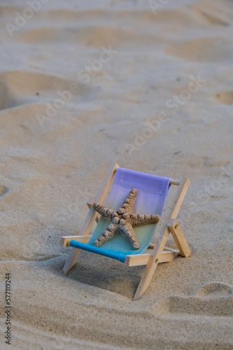 Fototapeta Naklejka Na Ścianę i Meble -  Sunny holidays on the beach with sand beach accessories with sea shells and sea star. Sun lounger stand sea Ocean background. Wooden beach chairs. Summer holiday vacation concept. 