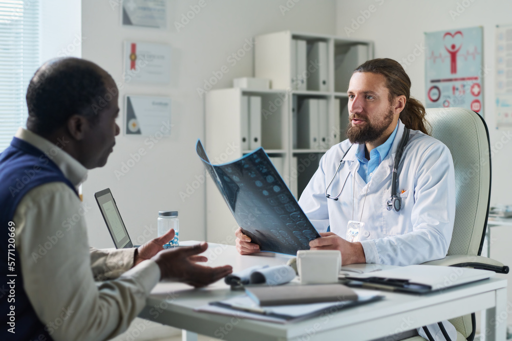 Obraz premium Serious clinician with result of mri scan of brain looking at senior patient during discussion of his diagnosis and giving medical advice