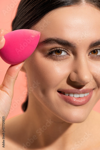 close up view of happy woman holding makeup sponge isolated on pink.