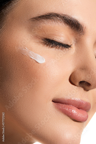 close up view of young woman with soft skin and cosmetic cream on cheek.