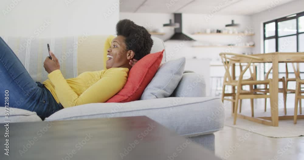 Happy african american woman laying on sofa using smartphone