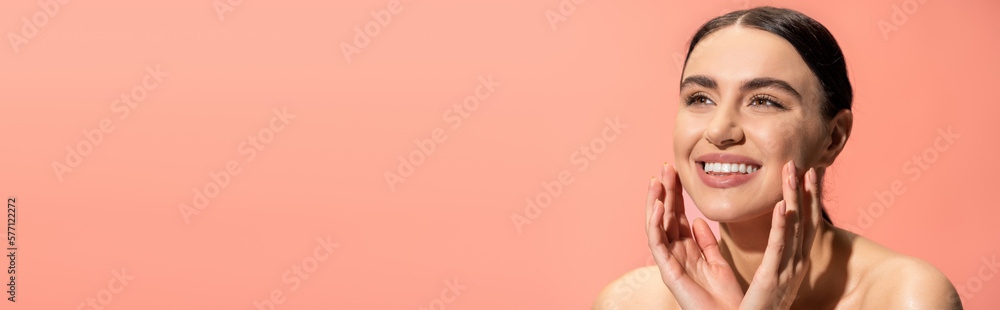 happy young woman with bare shoulders touching soft cheeks isolated on pink, banner. happy young woman with bare shoulders touching soft cheeks isolated on pink, banner.