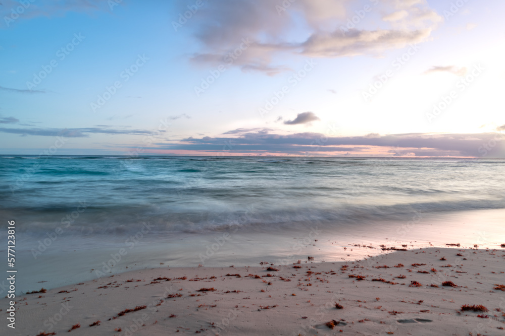 Long exposure of a pastel colored sunset with tranquil turquoise waves washing up on a beach in Barbados.	