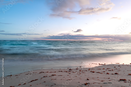 Long exposure of a pastel colored sunset with tranquil turquoise waves washing up on a beach in Barbados. 