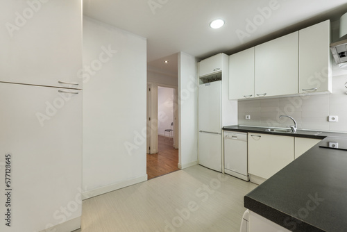 kitchen furnished with white wooden furniture with smooth doors with metal handles  black countertops and white appliances