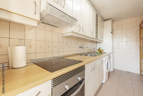 Kitchen with a wall covered in white cabinets with a wooden countertop and light tiles on the floors and walls