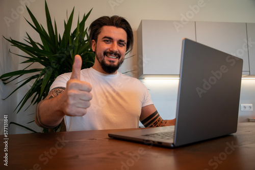 Handsome young man sitting in front of laptop showing thumbs up