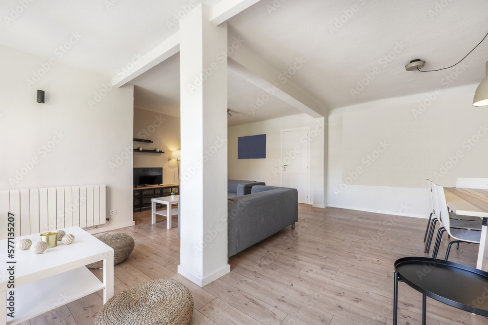 Fototapeta premium Living room of a holiday rental house with chestnut wood floors with natural fiber poufs, gray fabric sofas and a white square coffee table