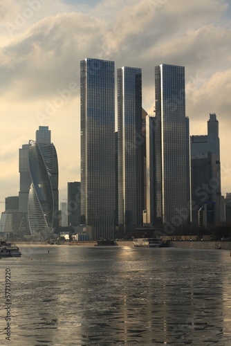 City landscape with a view of the Moscow City skyscrapers and a river with cracked ice in a frosty haze and sun rays on a frosty day.
