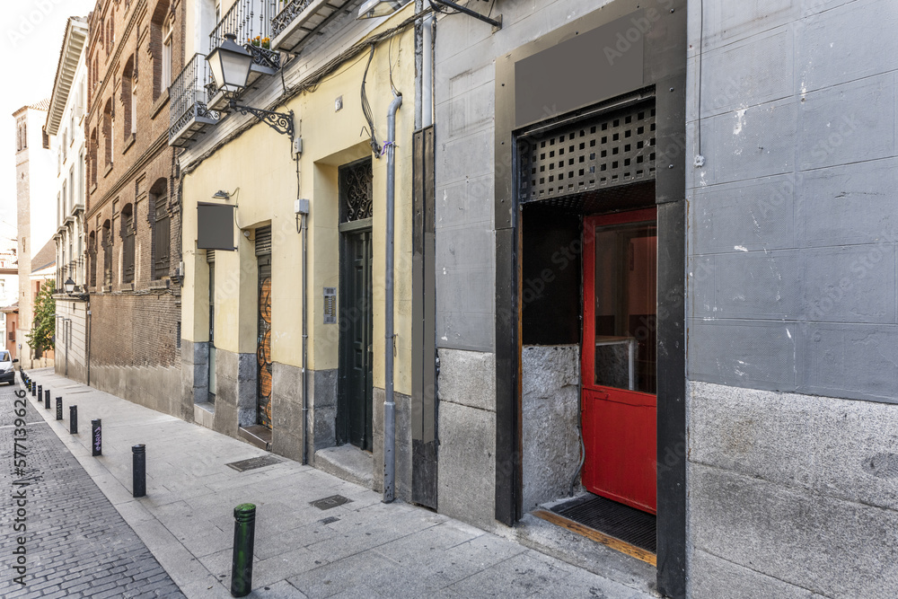 Fototapeta premium Entrance of a residential portal and a commercial premises in an old building with a granite facade in a central street with a cobblestone road and protection bollards