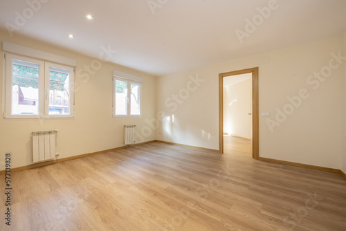 Empty room with wooden flooring, aluminum windows with radiators below with green awnings on the outside and oak joinery