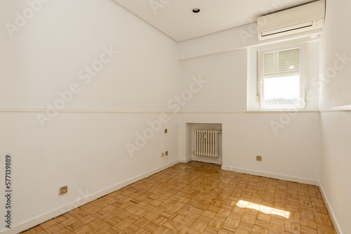 Empty room in an apartment with an oak parquet floor, an aluminum window, a radiator in a niche and an air conditioner on the wall © Toyakisfoto.photos