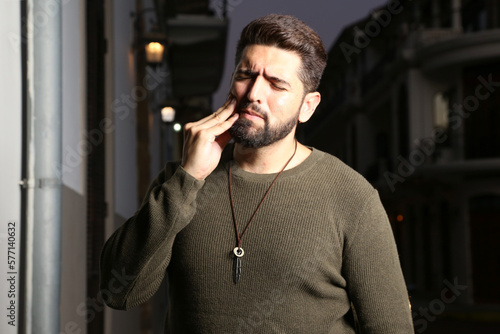 Man with a pained face due to toothache. Close-up photo of young man clutching his chin due to toothache. Man with pain in his face