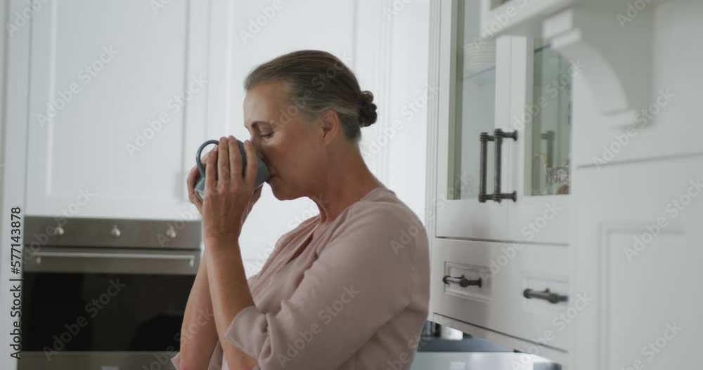 Senior caucasian woman wearing pink shirt and holding mug of coffee in kitchen