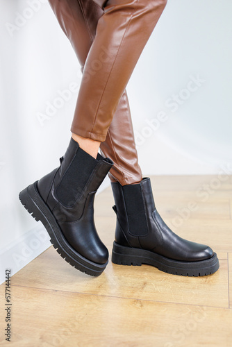 Slim female legs in black leather chelsea boots. Women's spring-autumn boots. Female legs in leather brown pants