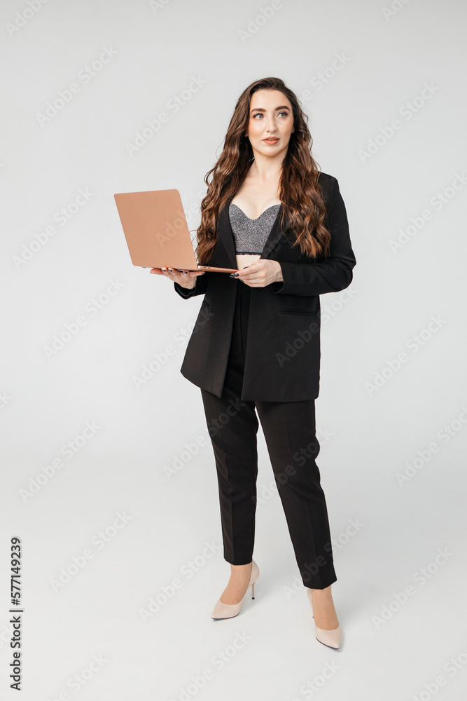 young businesswoman in a black jacket holds a laptop in her hands while standing on a gray background young businesswoman in a black jacket holds a laptop in her hands while standing on a gray background