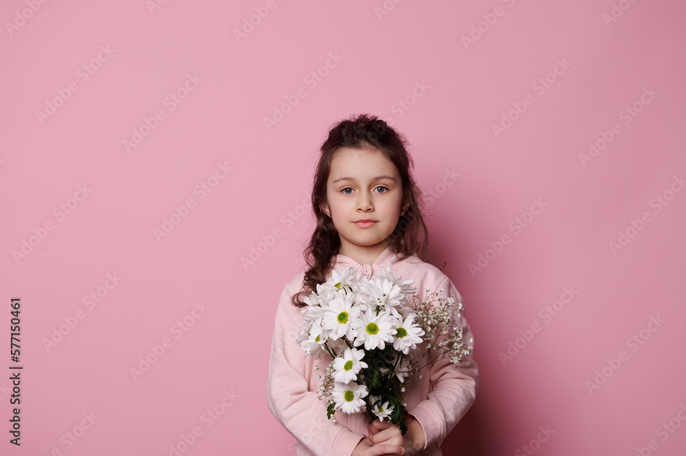 Isolated portrait on pink background of a charming little girl with bouquet of white flowers in hands, looking at camera. Copy space for ads. International Children's, Women's or Mother's Day concept Isolated portrait on pink background of a charming little girl with bouquet of white flowers in hands, looking at camera. Copy space for ads. International Children's, Women's or Mother's Day concept