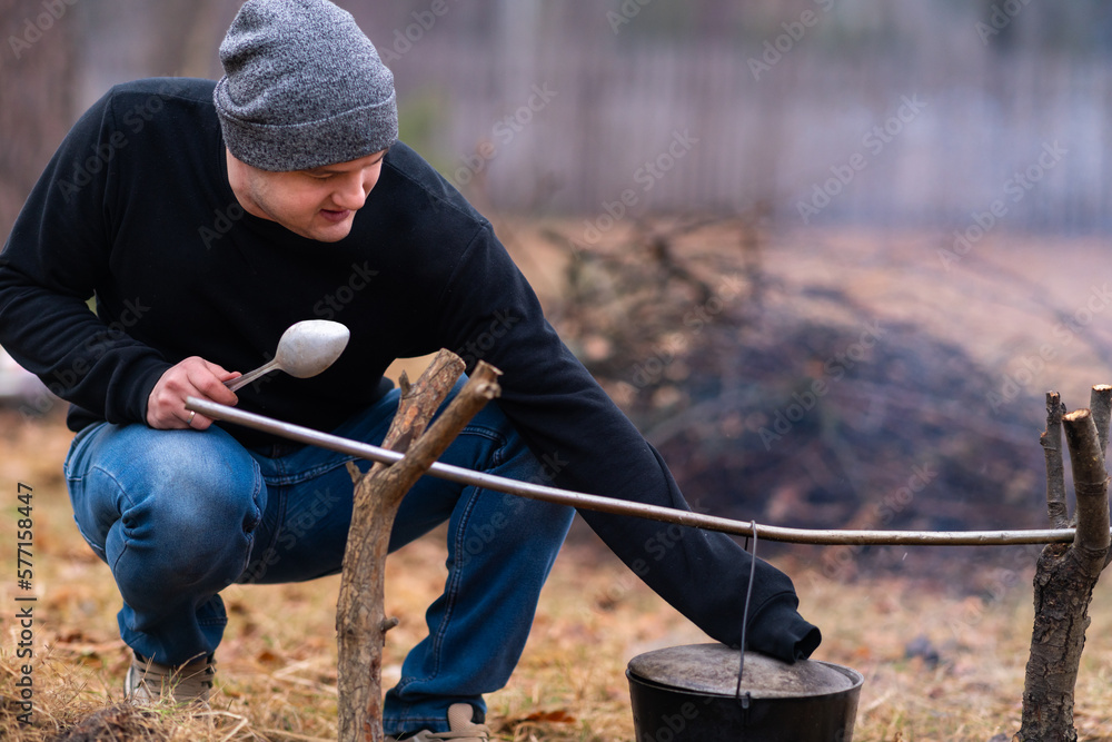 The guy lifts the lid of the cauldron hanging over the campfire