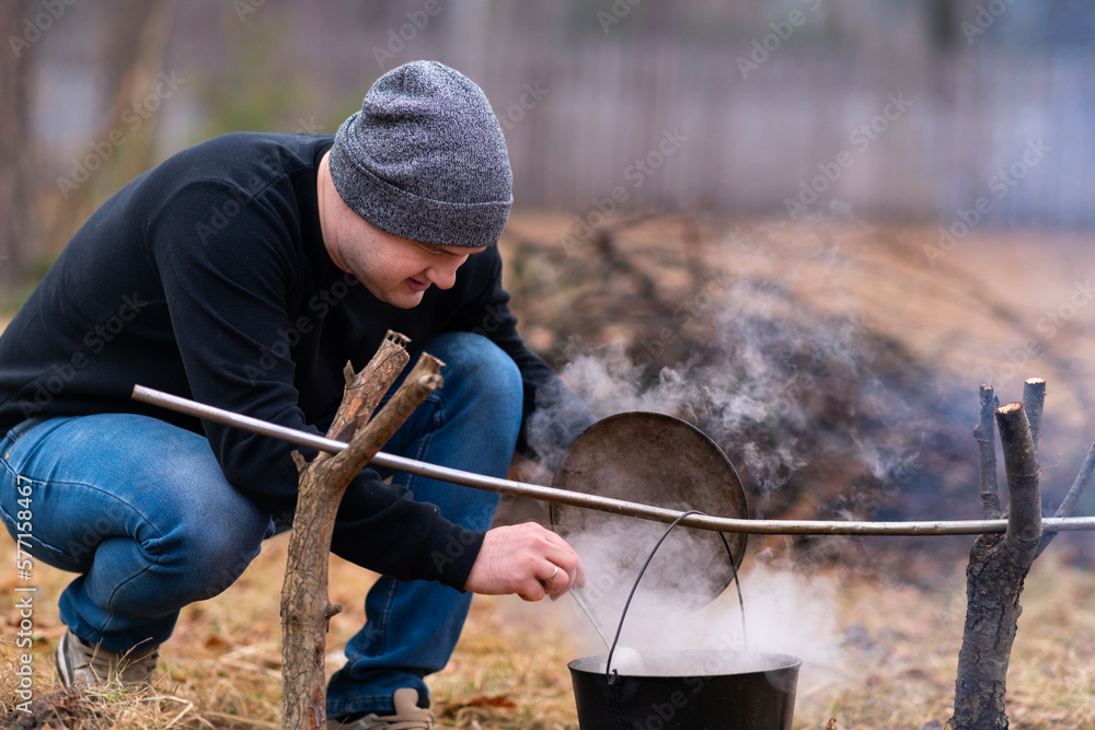 Young man stirs soup in a cauldron
