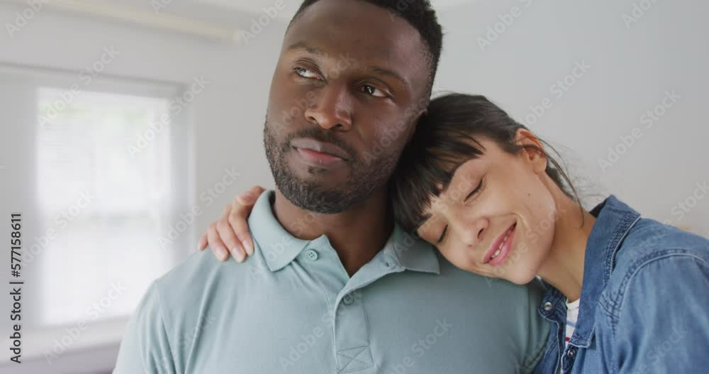 Portrait of happy diverse couple wearing jacket and shirt and embracing in living room Portrait of happy diverse couple wearing jacket and shirt and embracing in living room