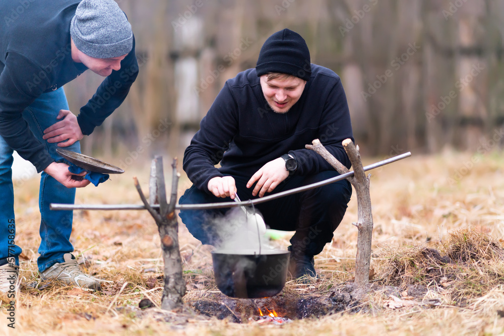 Two guys in nature in the process of cooking food on a fire