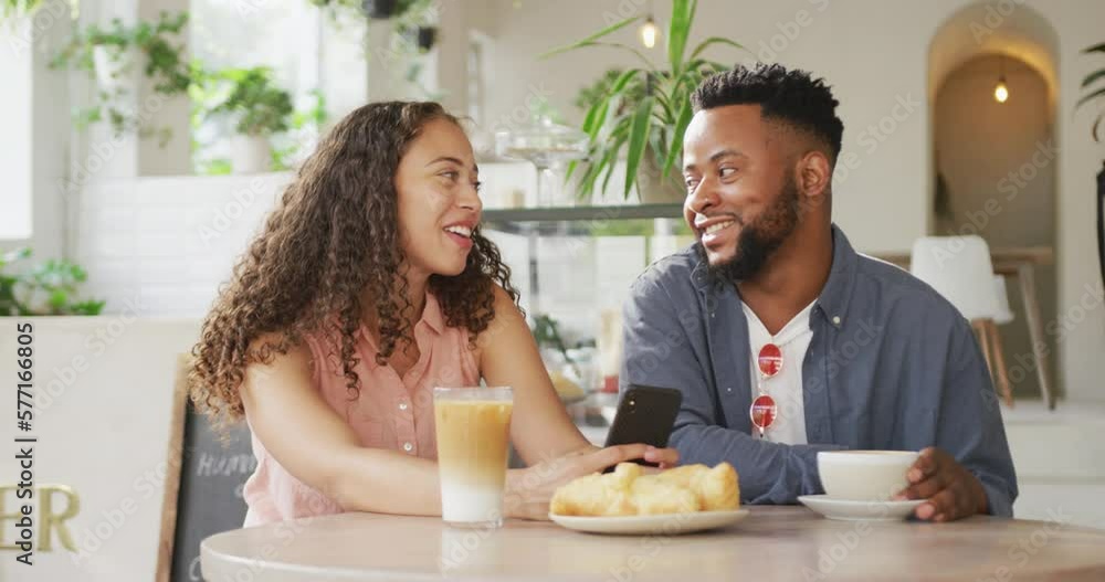 Happy diverse couple spending time together at cafe, drinking coffee and using smartphone Happy diverse couple spending time together at cafe, drinking coffee and using smartphone