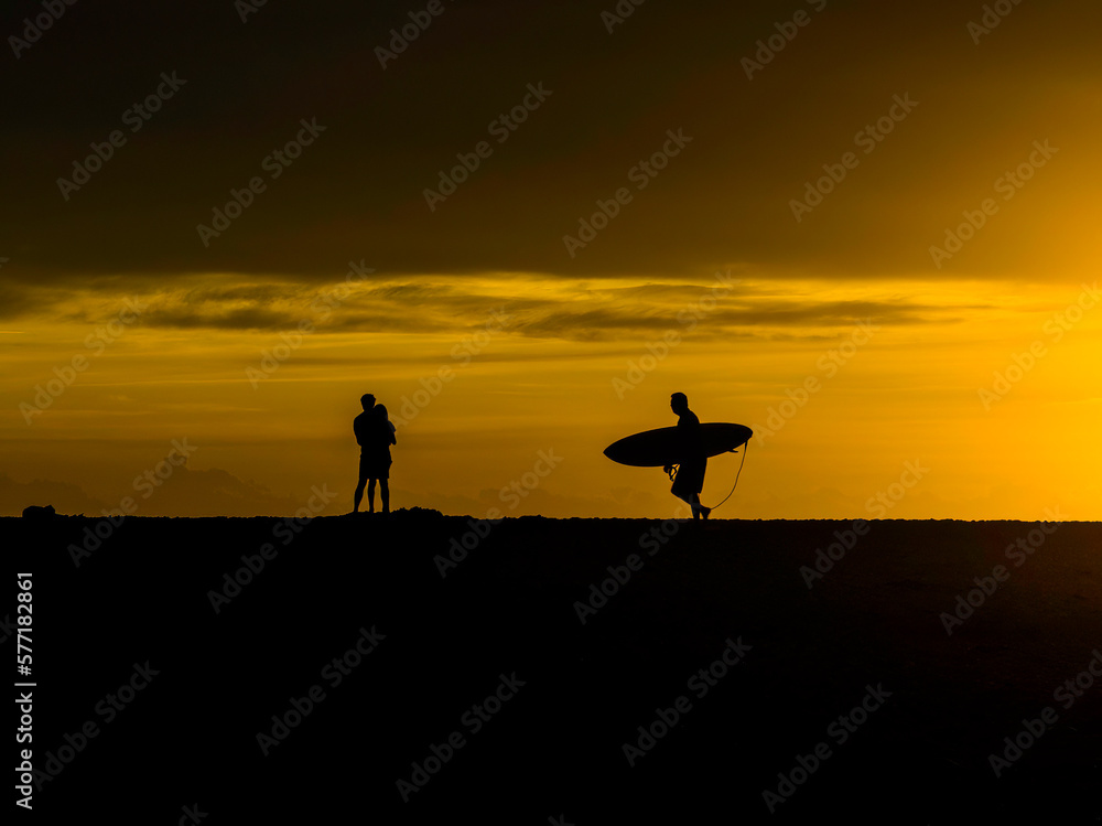 Sunrise silhouettes - lovers and a lone surfer heading out