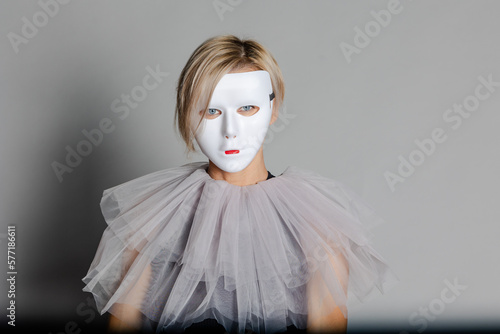 Face behind mask. Woman in white theater mask and harlequin collar on gray background. Fancy dress, masquerade clothes photo