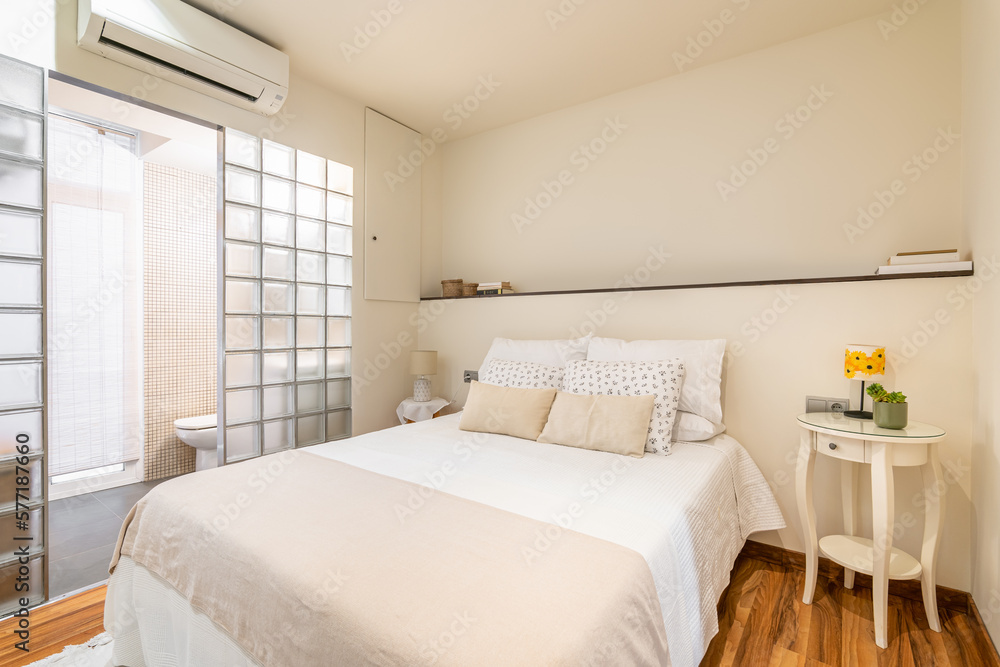 Cozy white bright small bedroom with bed and glass block wall with private toilet with vanity and air conditioning. Hotel room concept. Honeymoon Budget Room Cozy white bright small bedroom with bed and glass block wall with private toilet with vanity and air conditioning. Hotel room concept. Honeymoon Budget Room