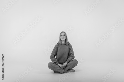 Portrait of a smiling young pretty European woman relaxing while sitting on the floor in jeans and a white shirt, isolated on white background. Place for writing