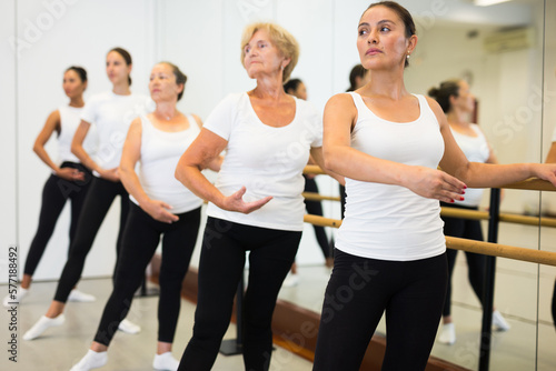 Women of different ages exercising ballet moves in training room.