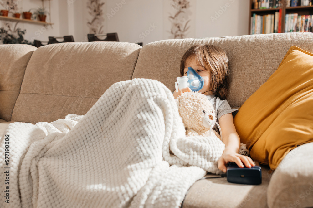 Little boy makes inhalation with a nebulizer at home lying on the couch. Cough prevention and treatment at home Little boy makes inhalation with a nebulizer at home lying on the couch. Cough prevention and treatment at home