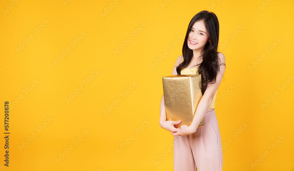 Excited Asian woman embraces gold gift box receive form lover on yellow background. Happy smile young cute girl holding surprise golden gift reward close eye passion cheerful celebration over isolated Excited Asian woman embraces gold gift box receive form lover on yellow background. Happy smile young cute girl holding surprise golden gift reward close eye passion cheerful celebration over isolated