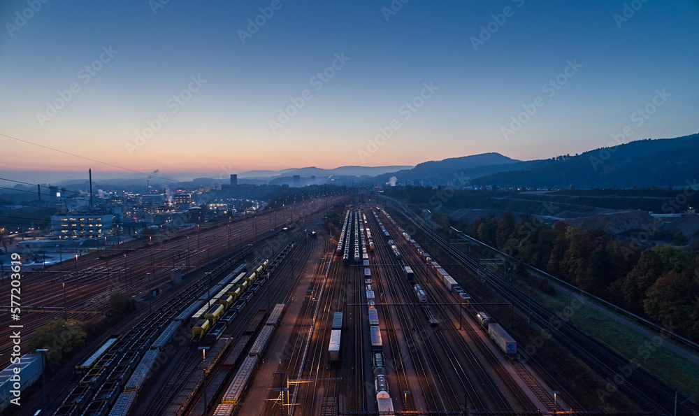 Güterbahnhof mit Wagons auf Abstellgleisen im Industrieviertel. Morgendämmerung, blaue Stunde und Morgenrot am Horizont.