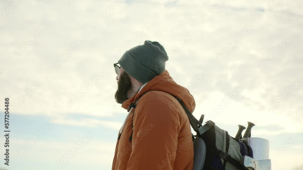 Bearded man with a backpack in sunglasses and warm clothes against the background of winter mountains and forest. The concept of hiking and active lifestyle. Bearded man with a backpack in sunglasses and warm clothes against the background of winter mountains and forest. The concept of hiking and active lifestyle.