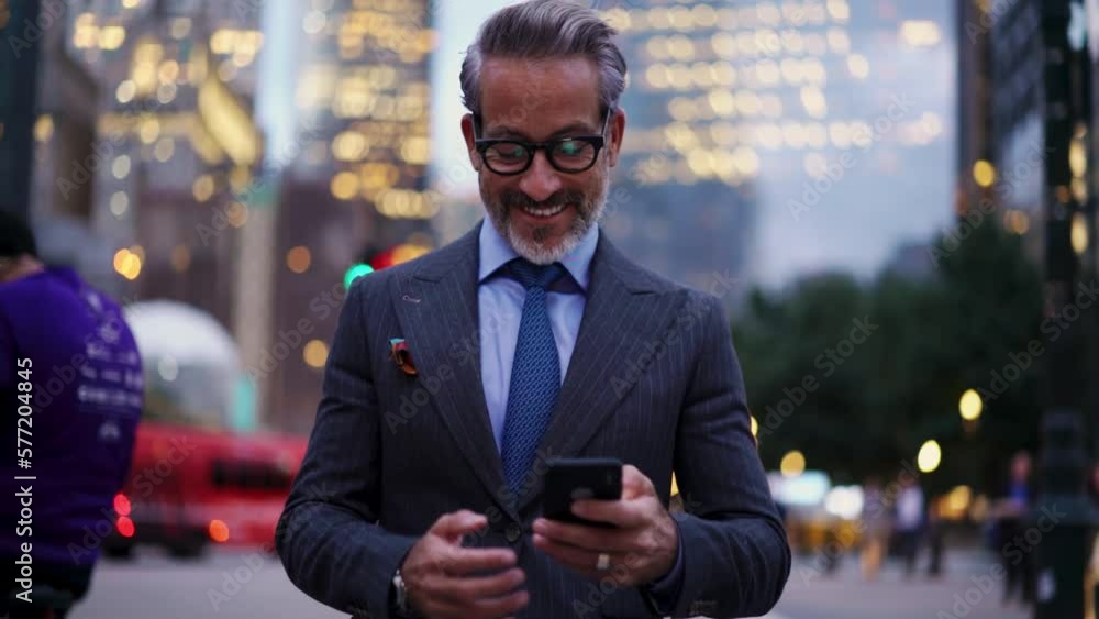 Adult and Happy successful business man in expensive suit, stylish eye glasses walks down street of New York, he feels confident. 50 years old male use mobile phone device while smiling and rejoices