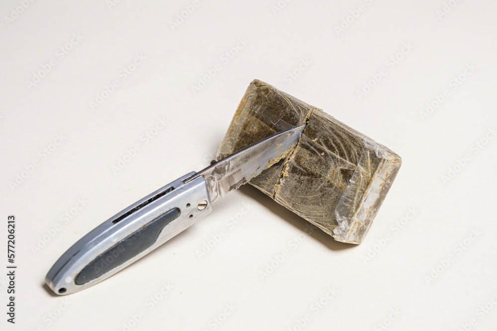 Hashish stick with a knife stuck ready for sale on a white background. Medical marijuana extraction dry hashish cannabis pollen. Hashish stick with a knife stuck ready for sale on a white background. Medical marijuana extraction dry hashish cannabis pollen.
