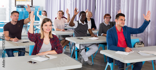 Group of adult people studying together in classroom, raising hands to answer