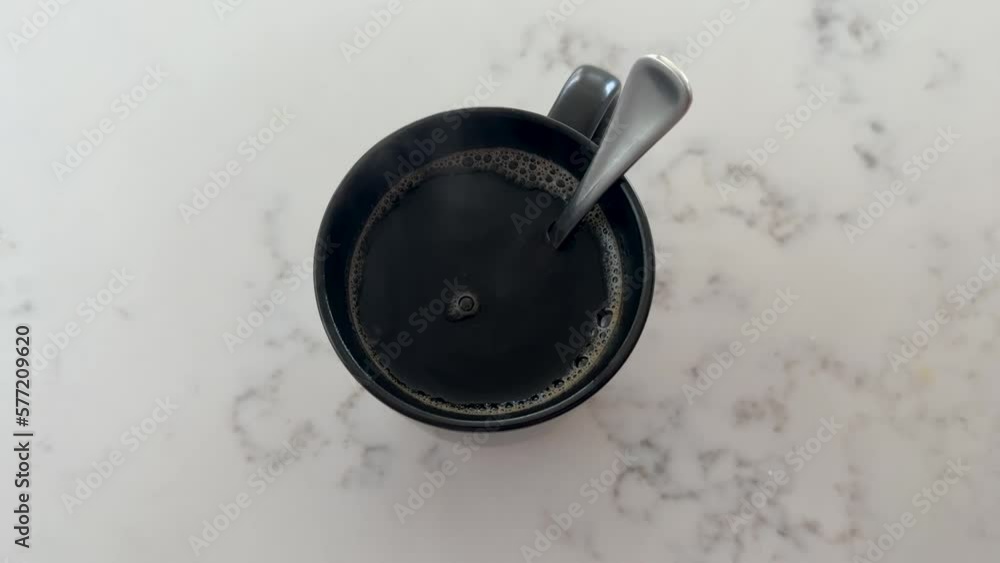 A teaspoon of stirred black coffee in a mug on the table. Top view A teaspoon of stirred black coffee in a mug on the table. Top view