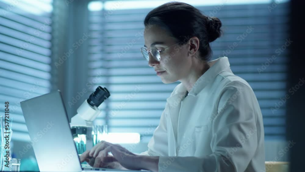 Medium shot of female scientist in lab coat typing on laptop while working at desk in laboratory Medium shot of female scientist in lab coat typing on laptop while working at desk in laboratory