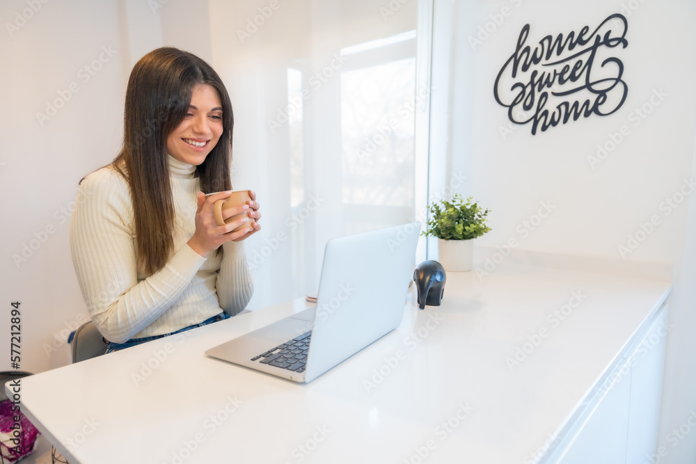 Businesswoman working on a computer with a coffee in her hand, business, home office, telecommuting Businesswoman working on a computer with a coffee in her hand, business, home office, telecommuting
